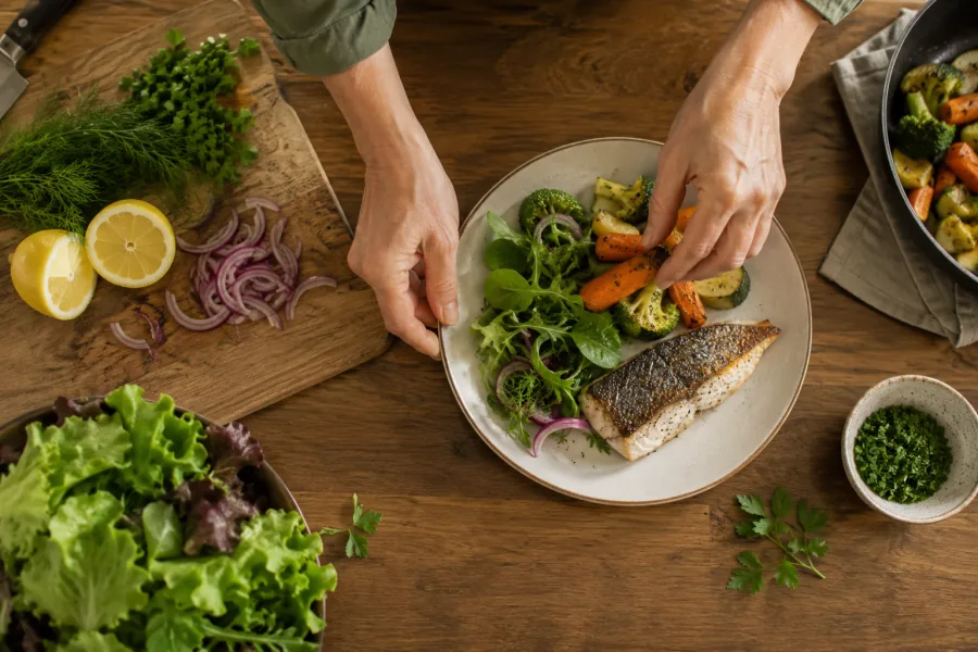 Plating a freshly cooked meal of fish, salad and roasted vegetables